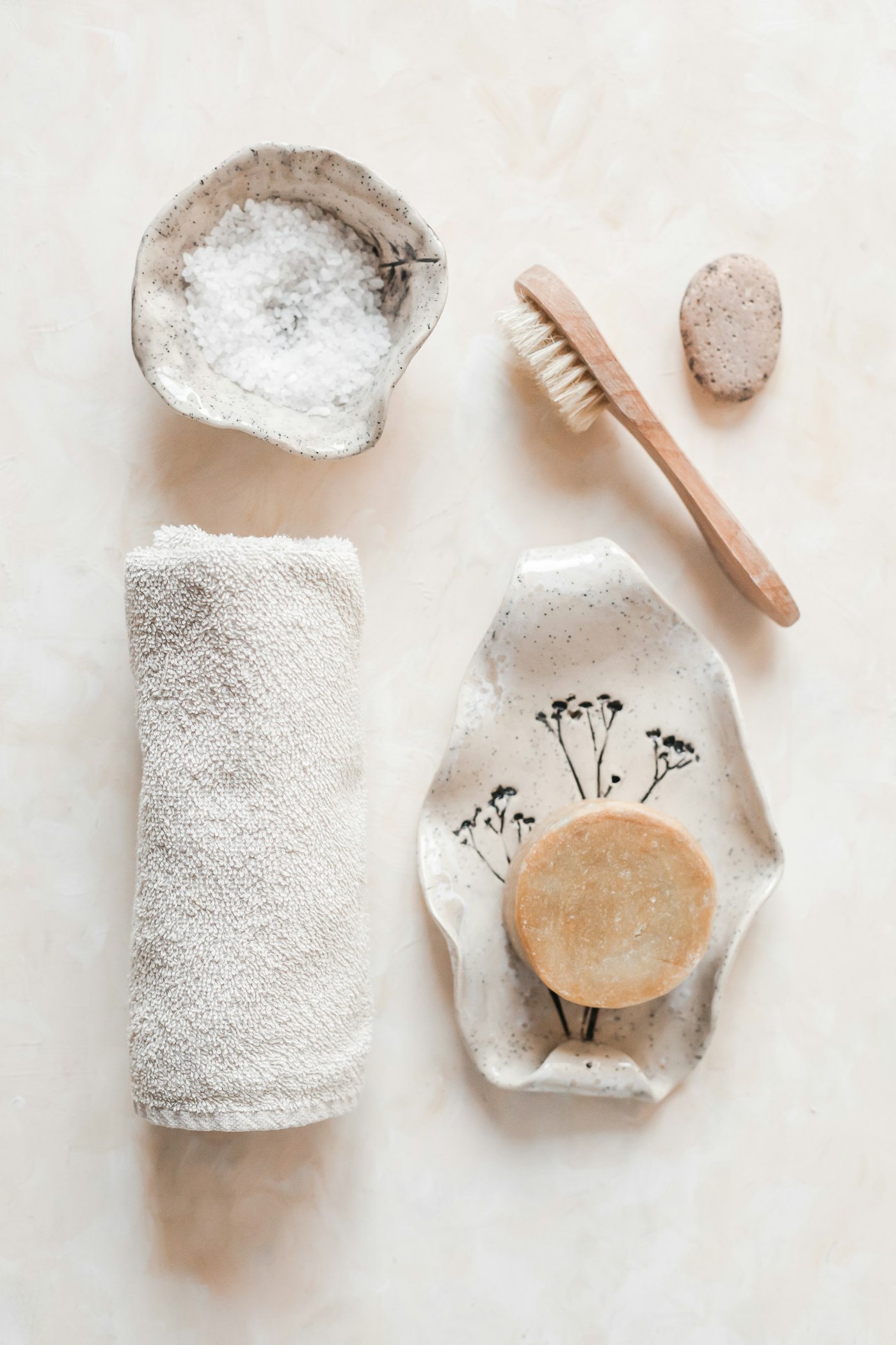 A folded towel, body brush and botanical soap arranged on a ceramic dish